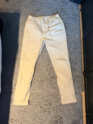 Beige chinos från Morris - Snygga beige chinos från Morris med avslappnad passform och resår i midjan samt dragsko. Tillverkade i mjukt bomullstyg som ger en skön känsla. Klassisk design med raka ben och diskreta fickor. Perfekta för en stilren och bekväm look.