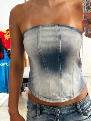 Ljusblå denim korsett-topp från Zara - Säljer en snygg ljusblå korsett-topp i denim med markerade sömmar och dragkedja bak. Toppen är axelbandslös och har en croppad passform. Nypris ligger på omkring 320kr och säljer för 150!💕 