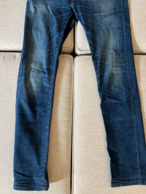 Blå jeans från tramarossa - Säljer ett par klassiska blå jeans med raka ben och snygga slitningar. Jeansen har knäppning med silverfärgade knappar och kontrastsömmar. Materialet är denim i bomull och passformen är avslappnad men ändå stilren.