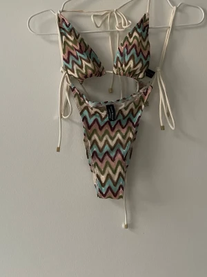 Mönstrad bikini från South Beach - Säljer en färgglad bikini från South Beach med zigzag-mönster i grönt, rosa, blått, beige och brunt. Bikinin har trekantsöverdel och knyt i sidorna samt i nacken. Materialet är polyester och elastan, perfekt för strandhäng i sommar!