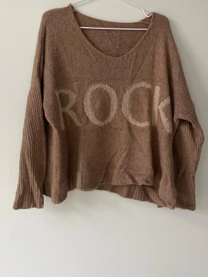 Brun oversized stickad tröja ROCK - Säljer en brun oversized stickad tröja med texten 'ROCK' i beige framtill. Köpt för 700kr.