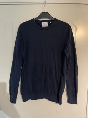 Mörkblå bomulls stickad tröja från Bläck - En stilren mörkblå stickad tröja med rund halsringning och ribbade muddar vid ärmslut och nederkant. Riktigt snygg passform och marinblå färg!🙌 Mycket bra skick, ser bara lite skrynklig ut.