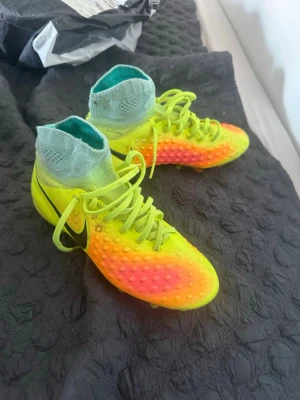 Nike fotbollsskor - Säljer ett par grymma fotbollsskor från Nike i neonfärger med cool sockliknande mudd. Skorna är gula med orange och rosa detaljer, har svarta Nike-loggor och knottrig yta för bättre bollkontroll. Perfekta för dig som vill sticka ut på planen! Nike magista elite