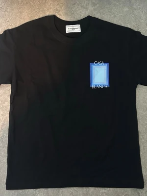 Svart Casa Blanca t-shirt med blå print - Snygg svart t-shirt från Casablanca med blått grafiskt tryck och texten 'Casa Blanca' både fram och bak. Klassisk passform och rund hals. Perfekt för dig som gillar stilrena men ändå unika plagg.