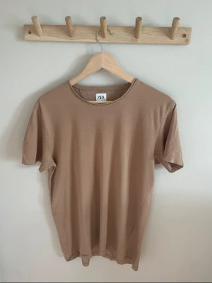 Beige t-shirt från ZARA - En stilren brun/beige t-shirt från ZARA med rund halsringning och klassisk passform. T-shirten är i ett tunt tyg, perfekt för sommaren! Storleken är true to size. Använd vid ett tillfälle.
