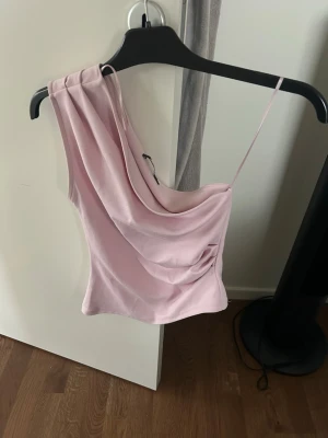 Ljusrosa oneshoulder topp Gina Tricot - Trendig ljusrosa oneshoulder topp från Gina Tricot med draperad framsida och smal axelrem. Perfekt för dig som vill ha en unik och stilren look. Tillverkad i mjukt material som känns skönt mot huden.