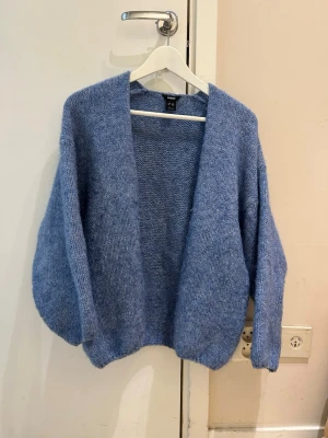  Trendig Blå stickad kofta med lös passform - Mysig blå stickad kofta med öppen front och avslappnad, oversized passform. Koftan har breda ärmar och ribbade muddar vid nederkant och ärmslut. Perfekt att slänga över en t-shirt för en chill look.