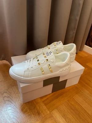 Valentino sneakers - Säljer valentino garavani skor, rockstud 11 med guld färgade nitar. Väldigt fina och passar till de mesta, sommar skor som passar perfekt nu till sommaren, allt medföljer som på bild. Box och påse. Va snabb me beställningar, alla storlekar finns inne, för frågar är det bara att höra av sig, kika även in våra omdömen🥰