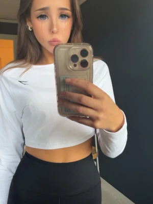 Vit croppad långärmad topp gymshark  - Säljer en vit croppad långärmad topp med rund hals och diskret logga på bröstet. Perfekt till höga byxor eller tights. Materialet känns mjukt och stretchigt, vilket gör den bekväm att bära hela dagen.