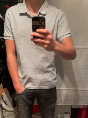 Ljusgrå pikétröja från J.Lindeberg  - Säljer en stilren ljusgrå pikétröja i bomull från J.Lindebergklassisk. Perfekt för en lite mer avslappnad men ändå stilren look. Modellen är 170cm och väger 64kg. Storlek M slimfit