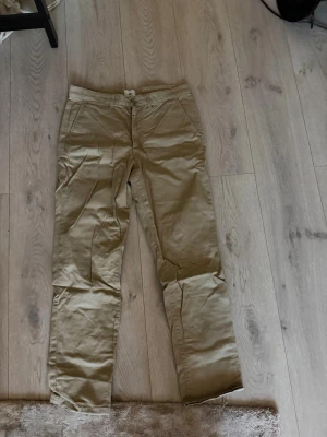 Beige chinos med raka ben - Snygga beige chinos med raka ben och klassisk passform. Byxorna har två sidofickor fram och två bakfickor med knapp. Tillverkade i ett mjukt och lätt bomullsmaterial som ger en avslappnad look. Perfekta för dig som gillar stilrena och bekväma byxor.