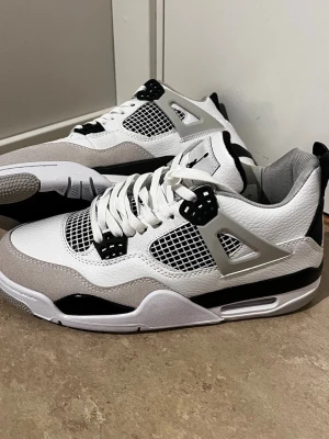Vita och grå sneakers med meshdetaljer - Snygga sneakers i vitt och ljusgrått med svarta detaljer. Ovandelen är i läder och mocka med meshpaneler på sidorna och tungan. Skorna har en chunky sula och coola plastdetaljer vid snörningen. Perfekta för dig som gillar streetwear och sportig stil.