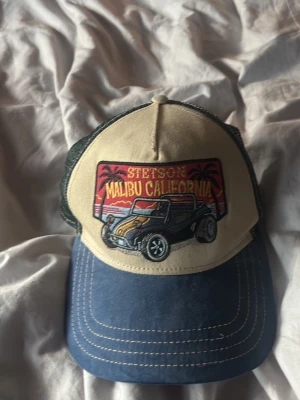 Stetson keps Malibu California - Cool keps från Stetson med broderad Malibu California-patch och bilmotiv. Framsidan är beige, skärmen blå och baksidan har grönt mesh-tyg för extra ventilation. Perfekt för en avslappnad och trendig stil.
