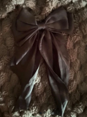 Stor svart hårrosett i satin - Snygg och stor svart hårrosett i glansigt satinmaterial. Rosetten har långa band och ger en elegant touch till din frisyr. Perfekt för att piffa upp håret med en trendig accessoar.