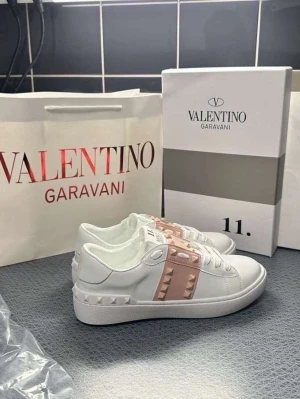 Valentino Rockstud Untitled sneakers - Snygga vita sneakers från Valentino med rosa band och ikoniska nitar över vristen. Skorna är låga och har en chunky sula samt coola detaljer i form av pyramidformade nitar runt hälen och på bandet. Perfekta för dig som vill sticka ut med exklusiv design.