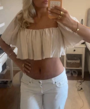 Beige offshoulder croppad topp - Säljer en beige/champange/ creme vit croppad topp med offshoulder och vida, korta ärmar. Toppen har en luftig och flowy passform, perfekt för varma dagar. Tillverkad i ett lätt tyg som känns skönt mot huden.
