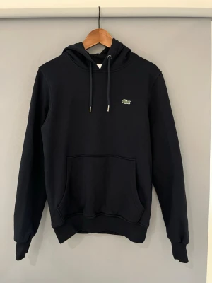 Mörkblå hoodie från Lacoste - Säljer hoodien då den inte kommer till användning längre. Storlek S. Inga defekter, använd en del hör av er vid minsta funderingar!