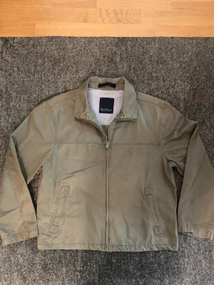 Beige vindjacka från McNeal - sitter som M-L. Stilren beige vindjacka från McNeal med dragkedja framtill och två snedställda fickor. Jackan har klassisk krage och är tillverkad i ett tunt, lätt material som passar perfekt för blåsiga dagar. Enkel och clean design som funkar till det mesta.