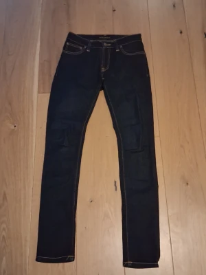 Mörkblå skinny jeans med kontrastsömmar - Snygga mörkblå/marinblå jeans från nudie jeans med en klassisk femficksmodell. Normal midja och tajtare ner till. Använt fåtal gånger då de snabbt blev för små för mig. Skick 9/10, lappen är lite förmörkad annars är inget fel. Kan ses på sista bilden!! Priset är inte stucket i sten, kan gå ner vid snabbt köp. Om du har några frågor skicka ett meddelande 😁