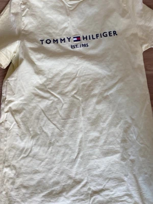 Gul slim fit t-shirt Tommy Hilfiger - Snygg gul t-shirt från Tommy Hilfiger i slim fit-modell. T-shirten har korta ärmar och klassisk rund halsringning. På bröstet finns ett broderat Tommy Hilfiger-logo med texten 'EST. 1985'. Perfekt till jeans eller shorts.