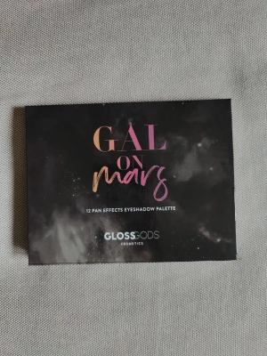 Gal on Mars ögonskuggspalett - Säljer en Gal on Mars ögonskuggspalett från Glossgods med 12 olika nyanser i metallic, skimrande och matta toner. Färgerna går i lila, rosa, guld, koppar, brons och rödorange. Paletten har spegel i locket och varje skugga har ett eget namn inspirerat av rymden. Skicket är otroligt bra, jag har använt på sin höjd 5 av skuggorna vid ett eller två tillfällen. Tanken var annars när jag införskaffade allt smink, men livet tog en vändning. Så ni köper en otroligt fin ögonskugga!😍