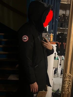 Svart goose parkas med huva - Säljer en svart goose parkas med huva och dragkedja samt knappar framtill. Jackan har en patch på ärmen och två stora fickor framtill. Lång modell som passar perfekt för kalla dagar. Snygg och stilren design. Det billiga priset beror på ett decimeter långt hål på insidan det påverkar inte så mycket enligt mig! Fråga gärna något!