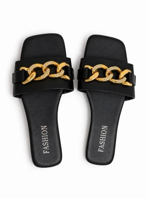Svarta sandaler med guldkedja - Stilrena svarta sandaler med bred rem och dekorativ guldfärgad kedja med glittrande stenar. Sandalerna har fyrkantig tå och platt sula, vilket ger en trendig look. Perfekta för dig som vill ha något extra till outfiten.