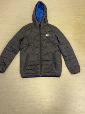 Jack & Jones jacka  - Snygg svart pufferjacka med huva och blått innerfoder. Jackan har dragkedja framtill, två sidofickor med dragkedja och quiltad design. Perfekt för kalla dagar och ger en sportig look. Enda problem är det som är på sista bilden.