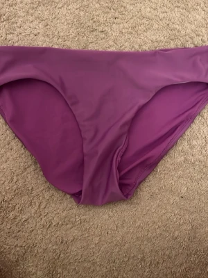 Lila bikiniunderdel i enkel design - Säljer en stilren lila bikiniunderdel med klassisk passform. Materialet är mjukt och stretchigt, perfekt för lata dagar på stranden eller vid poolen. Enkel och snygg modell som är lätt att matcha med olika överdelar.