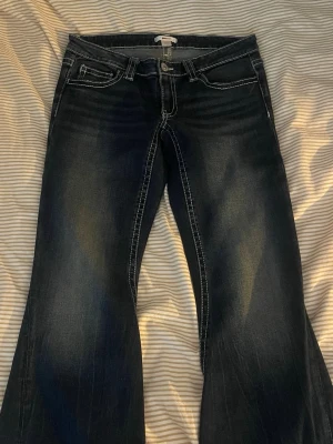 Mörkblå bootcut jeans med kontrastsömmar - Säljer ett par mörkblå bootcut jeans med snygga kontrastsömmar och slitningar framtill. Jeansen har klassisk femficksmodell och normal midja. Perfekta för dig som gillar en avslappnad men trendig look.