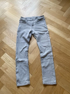 Ljusgråa jeans - Snygga ljusgrå jeans med rak passform och klassisk femficksdesign. Jeansen har bälteshällor och stängs med knapp och dragkedja. Perfekta för en clean och stilren look. Materialet ser ut att vara bomull med lite stretch.