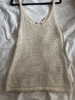 Stickad beige linnetopp - Säljer en stickad beige linnetopp med v-ringning och breda axelband. Toppen har en enkel och avslappnad look, perfekt för varma dagar. Materialet känns mjukt och luftigt, vilket gör den skön att bära till jeans eller kjol.