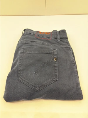 Dondup jeans - Snygga mörkgrå jeans i slim fit-modell med klassiska fem fickor och bälteshällor. Jeansen har en diskret detalj i form av en liten metallbokstav på bakfickan. Perfekta för en stilren och avslappnad look.