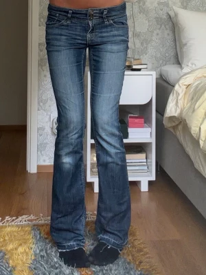 Blå bootcut jeans med låg midja - Säljer ett par blå bootcut jeans med låg midja. Passar perfekt inför hösten med den coola tvätten och för dig som vill ha dina egna unika jeans som inte alla andra har! Midjemått: 38cm, innerbenslängd: 83cm.