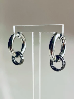 Silvriga hoops med svarta ringar i rostfritt stål  - Snygga örhängen i form av silvriga hoops med en extra svart ring hängande i varje. Runda och stilrena, perfekta för att ge din look en cool touch. Allergivänliga och designen är modern och enkel.