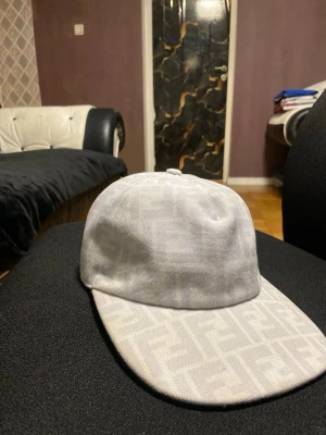 Fendi keps [vit] - Snygg vit keps från Fendi med det klassiska FF-mönstret över hela kepsen. Kepsen har böjd skärm och är tillverkad i ett tygmaterial som ger en exklusiv känsla. Perfekt för dig som vill ha en stilren accessoar med lyxig touch.