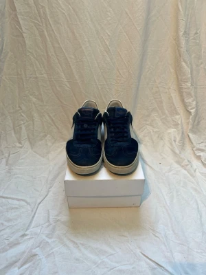 Marinblåa valentino flycrew - Snygga sneakers i marinblå mocka med vita detaljer på sidorna och vit sula. Skorna har klassisk låg profil och mörkblå snörning. Perfekta för dig som gillar stilrena och tidlösa sneakers med en sportig touch.