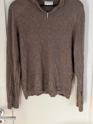 Brun halvzip tröja - Säljer en brun långärmad tröja med halvzip och ribbade muddar. Tröjan har en enkel och stilren design, perfekt för lager på lager och funkar till många olika outfits. Materialet ser ut att vara mjukt och bekvämt.