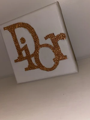 Canvas med texten 'Dior'  - En egen gjord bedazzlad tavla med motiv av loggan 'Dior'. Den är i en champagne/guldfärg. Canvasen är måtten 12x12cm.                                     Pris kan diskuteras