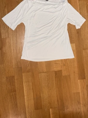 Vit offshoulder topp - Säljer en enkel och stilren vit offshoulder topp med korta ärmar. Toppen har en mjuk och följsam passform och är perfekt för dig som gillar minimalistisk stil. Materialet känns lätt och bekvämt mot huden.