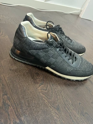 Svarta Louis Vuitton sneakers - Snygga svarta sneakers från Louis Vuitton med stickad ovandel och detaljer i läder. Skorna har en diskret logga på hälen och en vit sula som kontrast. Perfekta för dig som vill ha en exklusiv och stilren look.