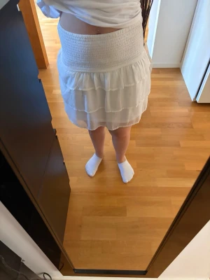 Vit kort volangkjol  - Söt vit kortkjol med bred smockresår i midjan och flera lager volanger. Kjolen har en luftig och lätt känsla, perfekt för varma dagar. Materialet känns som tunn polyester eller bomull och ger en flowy look. Skriv pm vid funderingar!☺️