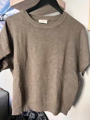 Beige stickad topp från Freequent - Snygg beige stickad topp från Freequent med korta ärmar och rund halsringning. Tröjan har ribbade detaljer vid hals, ärmslut och nederkant. Perfekt för lager på lager och enkel att matcha med olika stilar.