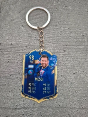 Nyckelring med Messi FIFA-kort - Säljer en unik nyckelring med motiv av Messi från FIFA Ultimate Team. Kortet är blått och guld med detaljerade stats och PSG-logga. Perfekt accessoar för fotbollsfans som vill ha något personligt på nyckelknippan.
