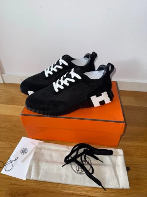 H skor - Snygga svarta sneakers med vit sula och vita skosnören. Skorna har en tydlig vit H-detalj på sidan och är tillverkade i en mix av mesh och mocka. Kommer med extra skosnören och dustbag. Perfekta för dig som gillar stilrena och moderna sneakers.