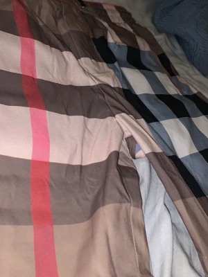 Rutiga shorts i beige och svart - Snygga shorts med klassiskt rutigt mönster i beige, svart, vitt och röda detaljer. Perfekta för sommaren och har en avslappnad passform. Tillverkade i ett mjukt bomullsliknande material som känns skönt mot huden.