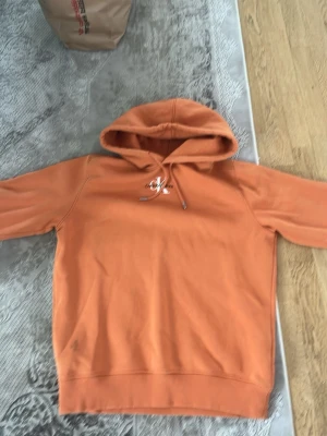 Orange hoodie från Calvin Klein - Snygg orange hoodie från Calvin Klein med klassisk CK-logga på bröstet. Hoodien har dragsko i huvan och ribbade muddar vid ärmar och nederkant. Perfekt för en avslappnad och trendig look.