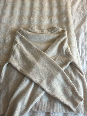 Vit stickad tröja - hm  - Mysig beige stickad tröja med rund halsringning och långa ärmar. Tröjan har ribbade muddar vid ärmslut och nederkant, vilket ger en klassisk och enkel look. Perfekt för lager på lager under kyliga dagar.