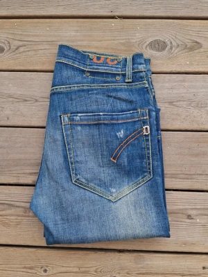 Dondup george  - Säljer ett par blå jeans med raka ben och snygga slitningar framtill och på bakfickan. Jeansen har kontrastsömmar och klassisk femficksdesign. Perfekta för en avslappnad och trendig look.