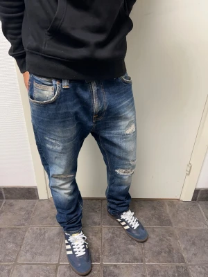 Nudie jeans - Ett par riktigt feta Nudie jeans i storlek 33/28. En liten fläck på höger ben, annars mycket bra skick. Modell: Brute Knut. A=45CM B=96CM C=16,5CM. Modellen är 173cm, 64kg. Pris kan diskuteras!!
